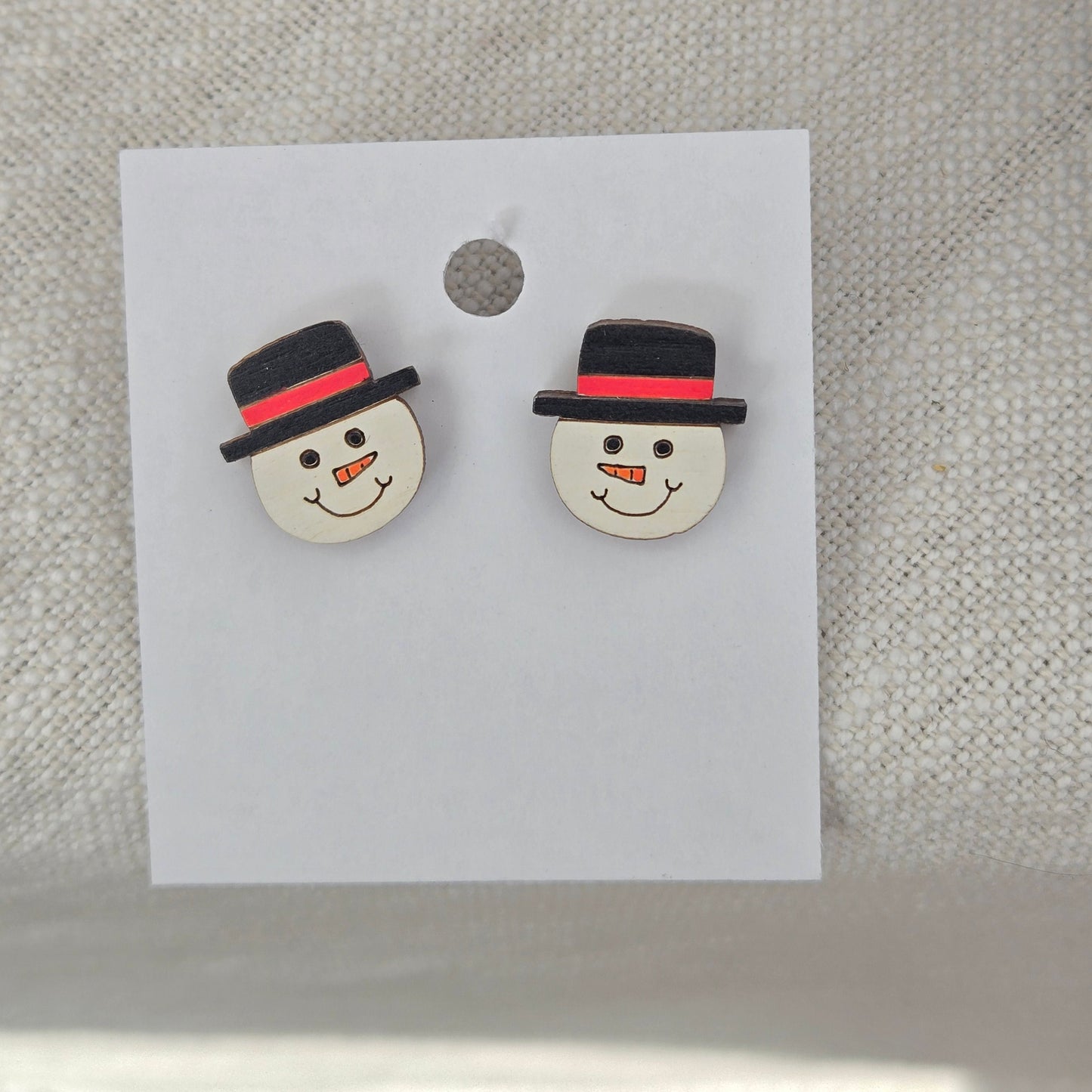 A pair of snowman face stud earrings displayed on a card.