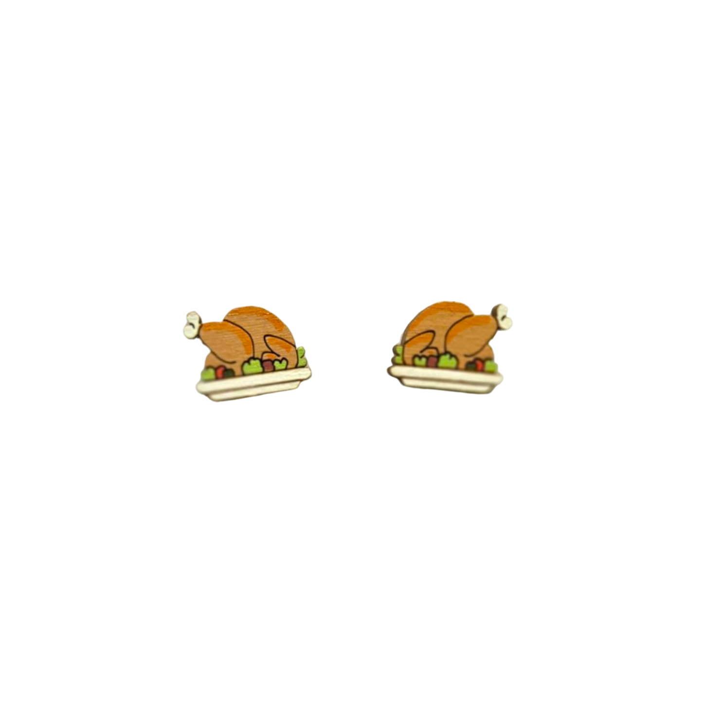 A pair of small stud earrings shaped like roasted turkeys sitting in white platters with green and red vegetables, shown on a plain white background.