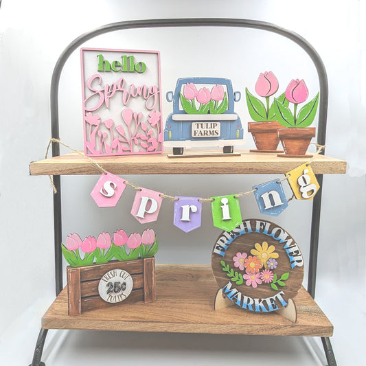 Seven-piece Spring tiered tray decoration set with tulips, truck, Spring banner, and floral sign. Laser cut and hand-painted with sizes up to 5 inches wide.